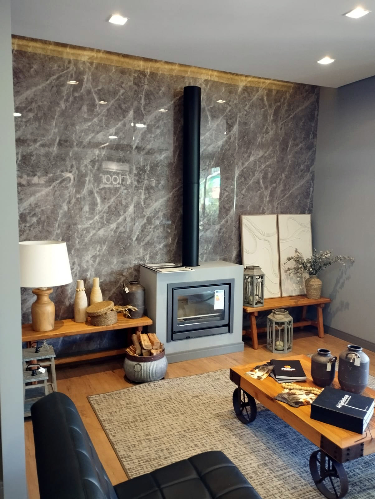 Sala de estar sofisticada com parede revestida em porcelanato cinza marmorizado e iluminação dourada embutida, lareira moderna, piso laminado amadeirado, móveis rústicos e poltrona de couro preto, mood elegante e acolhedor, fotografia de interiores realista