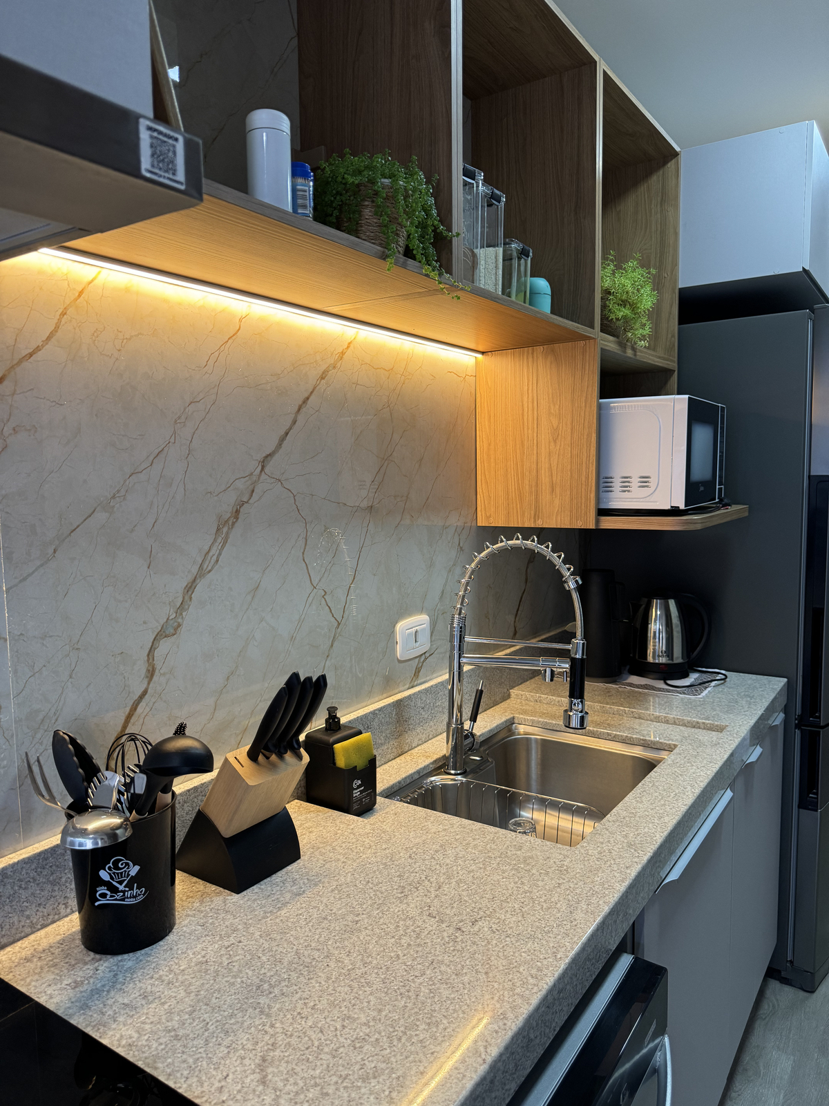 Cozinha contemporânea com bancada em granito claro, revestimento de parede em porcelanato bege marmorizado, armários planejados em madeira e cinza, iluminação LED embutida quente, cuba inox e torneira gourmet, fotografia de interiores realista